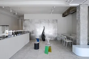 A modern interior design showroom with a white theme, featuring chairs, dining tables, and decorative vases in a clean and bright space
