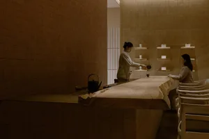 A woman cooks in a cozy kitchen with a wooden countertop, dining table, and various kitchen items, creating a warm and inviting atmosphere