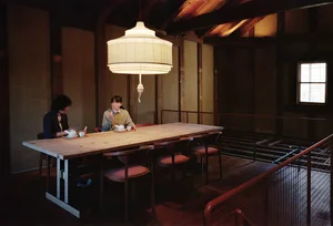 A warm and inviting Asian restaurant with wooden floors and walls, featuring a long dining table and smaller table in the background