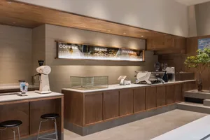 Warm and inviting coffee shop interior with wooden counters and cabinets, featuring a kitchen area with appliances and multiple cups