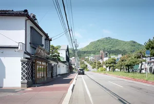 熱鬧的亞洲街景，白色建築頂著紅瓦屋頂，周圍有行人和停放的車輛，位於都市環境中