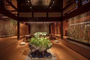 A serene indoor space with a large rock, plants, and wooden floor, featuring multiple benches for seating and a calm atmosphere
