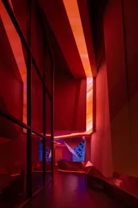 A modern museum gallery with a large red metal wall, two windows, and a contemporary design