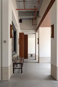A calm and quiet hallway with a concrete floor, featuring a bench, vases, and two chairs