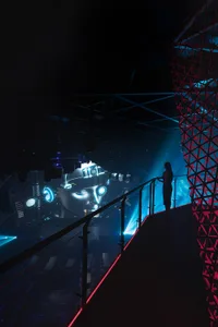 An indoor event venue with a large stage featuring a futuristic display, surrounded by attendees and a performer