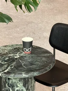 A modern indoor space with a marble table, a black chair, two cups, and a potted plant, featuring a sophisticated atmosphere
