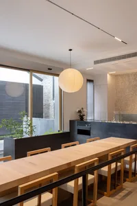 A dimly lit dining area with a large wooden table, chairs, potted plants, vases, and bowls, creating a warm and inviting atmosphere