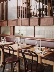Warm and inviting dining space with wooden tables, chairs, and decor, featuring wine glasses, utensils, vases, and potted plants