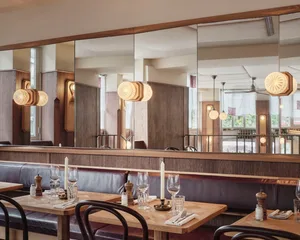 A cozy restaurant interior with wooden floors and walls, featuring multiple dining tables and chairs, wine glasses, and bottles, creating a warm and inviting atmosphere