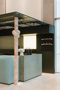 A modern interior design showroom with green and white walls, a marble pillar, and decorative items such as a coffee machine, vase, and bottles