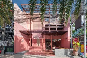 An open-air restaurant with a pink building, patio area, dining tables, and palm trees, creating a warm and inviting atmosphere