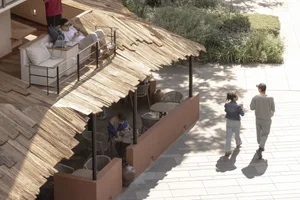 Outdoor restaurant with a thatched roof, tables, and chairs, surrounded by people dining and socializing