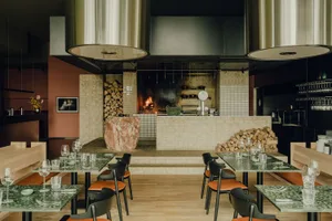A cozy restaurant dining area with a stone wall, fireplace, and dining tables with wine glasses, creating a warm and inviting atmosphere