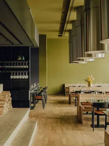An inviting restaurant with green walls, wooden floors, and dining tables, set with wine glasses, creating a comfortable atmosphere for guests