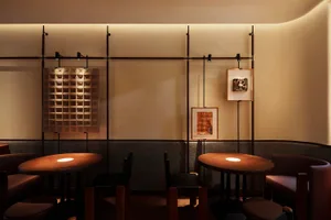 A cozy dining area with two round tables and three chairs, surrounded by artworks on the walls, in a restaurant or cafe setting