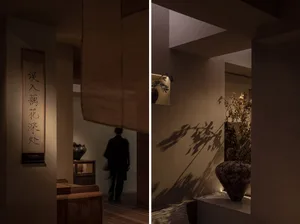 Warm and cozy interior space with wooden floors and walls, decorated with potted plants and vases, and a person walking in the hallway