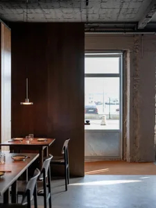 Modern restaurant interior with wooden floors and walls, featuring chairs and tables in a comfortable dining area