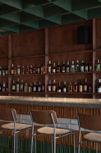 A warm and inviting bar area with wooden walls and a countertop, featuring bottles and wine glasses, and two chairs in the background