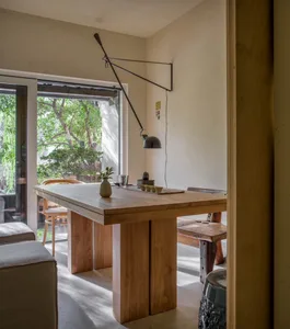 Open living space with a wooden dining table, chairs, and a couch, well-lit with natural and artificial light, creating an inviting atmosphere