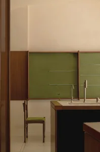 A clean and organized kitchen with green walls, white countertops, and two sinks, suggesting a nearby dining area