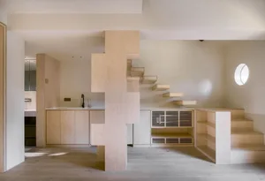Open modern living space with hardwood floors, wooden cabinets, and a central staircase, featuring a kitchen with a sink and refrigerator and a living area with a couch