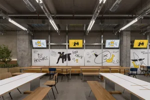 A modern room with white walls, featuring rows of tables and chairs, and writings and drawings on the walls