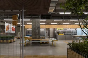 Modern industrial dining area with multiple tables and benches, cement pillar, and chairs, set in a large open space