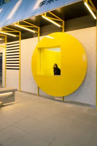 Interior space with a yellow circular window, a bench, and two people, featuring a warm and inviting atmosphere