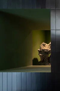 A serene interior space with a green wall and a stone countertop featuring two large rocks, creating a calm atmosphere