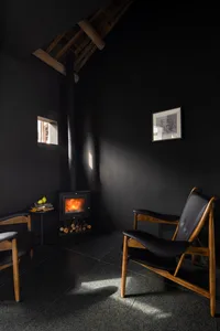 Cozy living room with a wood stove, two chairs, and a dining table, featuring a warm and inviting atmosphere