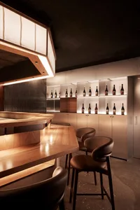 A bar area in a restaurant with a wooden countertop, wine bottles, and comfortable seating for patrons, creating a warm and inviting atmosphere