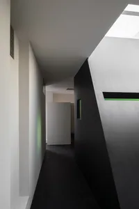 Narrow hallway with a black door, a white wall, and concrete walls, featuring an open and closed door