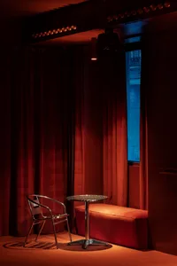 A warm and inviting room with a red curtain, a chair, a bench, and two dining tables, featuring a cozy atmosphere and elegant touches