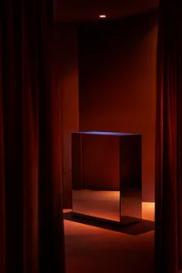 A room with a dark wood table and a large mirror in front of a curtain, creating a sophisticated atmosphere