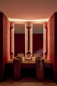 Bathroom with two sinks, wooden countertop, red wall, and mirrors, with personal care products scattered around