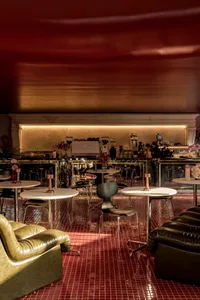 A warm and inviting restaurant interior with red walls, dining tables, chairs, and potted plants