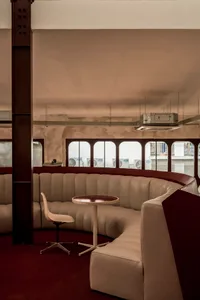 Modern living space with a circular seating arrangement, white couches, chairs, and a dining table, surrounded by red accent walls and natural light from windows