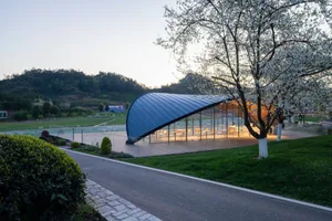 Bright and inviting open air space with a large glass wall, concrete or similar materials, and several chairs