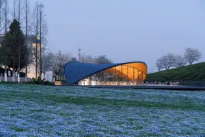 A modern building with a large dome on its roof, surrounded by chairs and dining tables, featuring a concrete exterior and sophisticated design