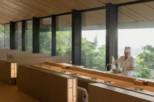 A bustling restaurant kitchen with a large window, sink, dining table, chairs, and people preparing food