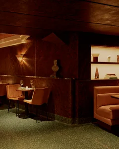 Cozy restaurant bar with brown walls and floors, featuring chairs, dining tables, wine glasses, and books in a relaxed atmosphere