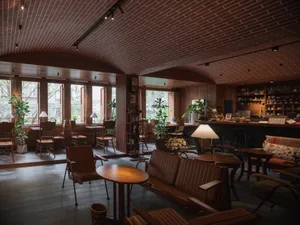 Cozy restaurant interior with wooden floors and walls, chairs, dining tables, and a potted plant