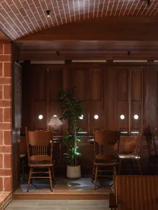 Warm and inviting dining space with wooden floors and walls, surrounded by potted plants and dining tables with chairs