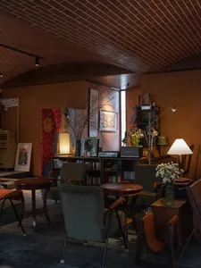 Cozy modern living space with a dining table, chairs, couch, and potted plant, featuring books and a lived-in feel