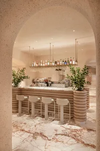 A restaurant bar with a wooden countertop, three chairs, and bottles on display, creating a welcoming atmosphere for customers