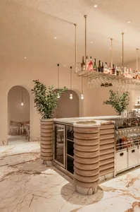 Modern bar area with a long counter, sink, and bottles, surrounded by chairs in a well-lit space with a focus on functionality and organization