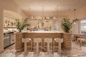 A modern bar area with a long counter, stools, and bottles, featuring a combination of white and brown elements