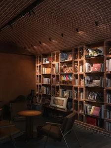 A cozy living space with a wooden bookshelf, brick-patterned surface, multiple chairs, and a dining table