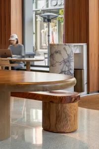 A modern dining space with a wooden table and chairs, surrounded by a restaurant setting with two people present
