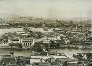 A black and white photo of a historic city with a mix of architectural styles, including Chinese architecture, featuring stone buildings and boats in the water